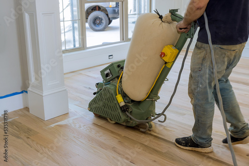 During of newly constructed house, floor sander is being used to grind down a wooden parquet floor