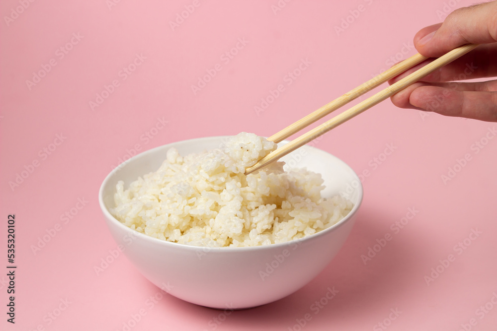The hand takes the boiled rice with chopsticks on a pink background. Traditional Asian food. The hand takes the boiled rice with chopsticks on a pink background. Traditional Asian food.
