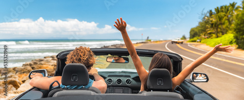 Road trip summer vacation fun young couple driving convertible car on holiday travel destination banner panoramic. Woman with arms up happy, man driver having fun.