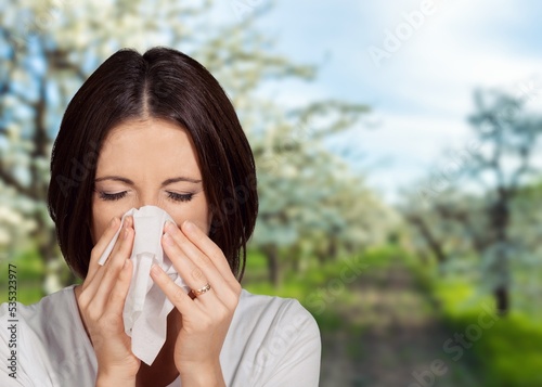 Young pretty woman blowing nose in front of blooming tree. Spring allergy concept. Sick people allergy or virus influenca concept.