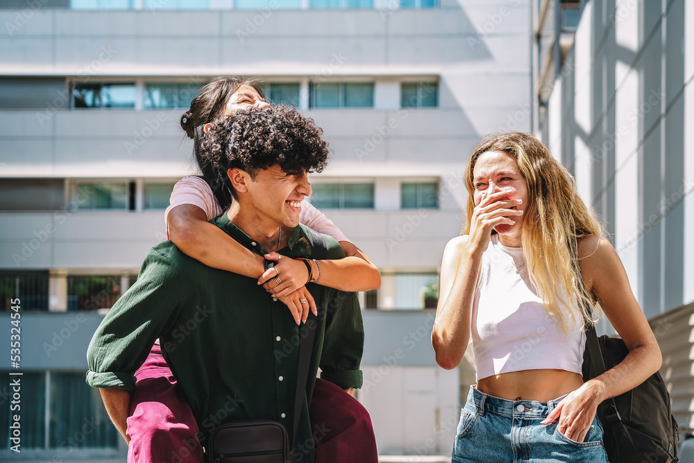 Joyful lady laughing near guy giving piggyback ride to girlfriend Joyful lady laughing near guy giving piggyback ride to girlfriend