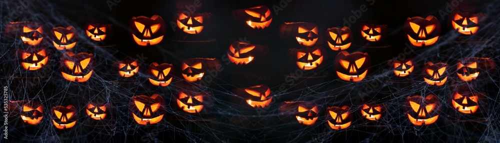 Scary Halloween celebration holiday card - Many spooky carved pumpkins and spider web on dark wooden wall background banner panorama. Scary Halloween celebration holiday card - Many spooky carved pumpkins and spider web on dark wooden wall background banner panorama.