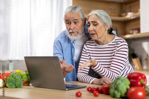 Confused Senior Spouses Suffering Problems With Laptop While Spending Time In Kitchen