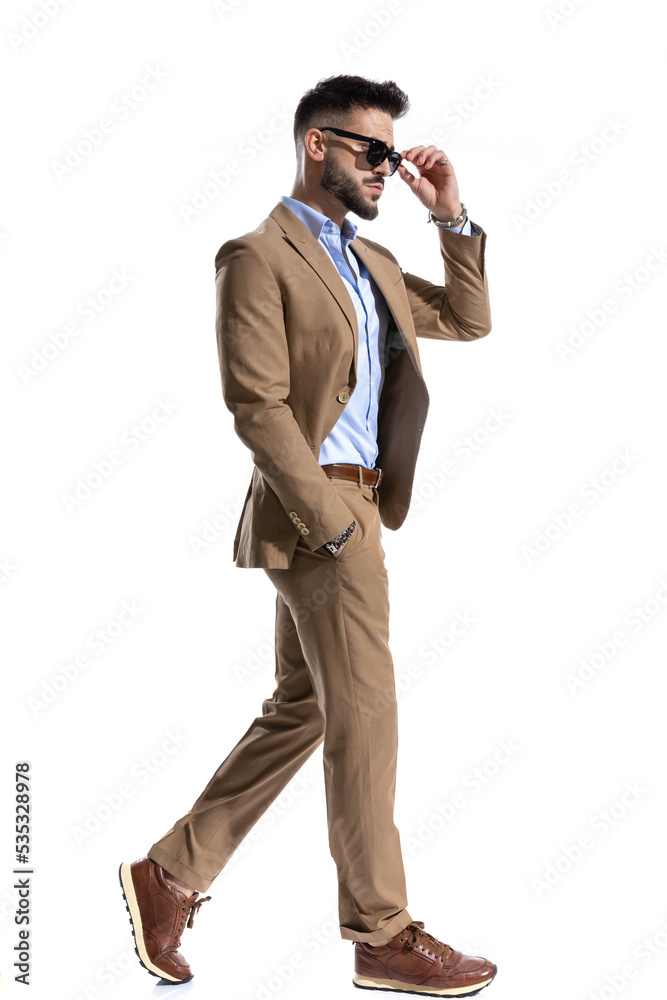 side view of young smart casual man adjusting glasses and walking side view of young smart casual man adjusting glasses and walking