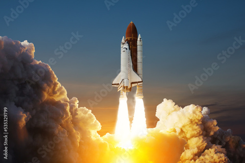 Fototapeta Naklejka Na Ścianę i Meble -  Spaceship lift off. Space shuttle with smoke and blast takes off into space on a background of sunset. Successful start of a space mission. Elements of this image furnished by NASA.