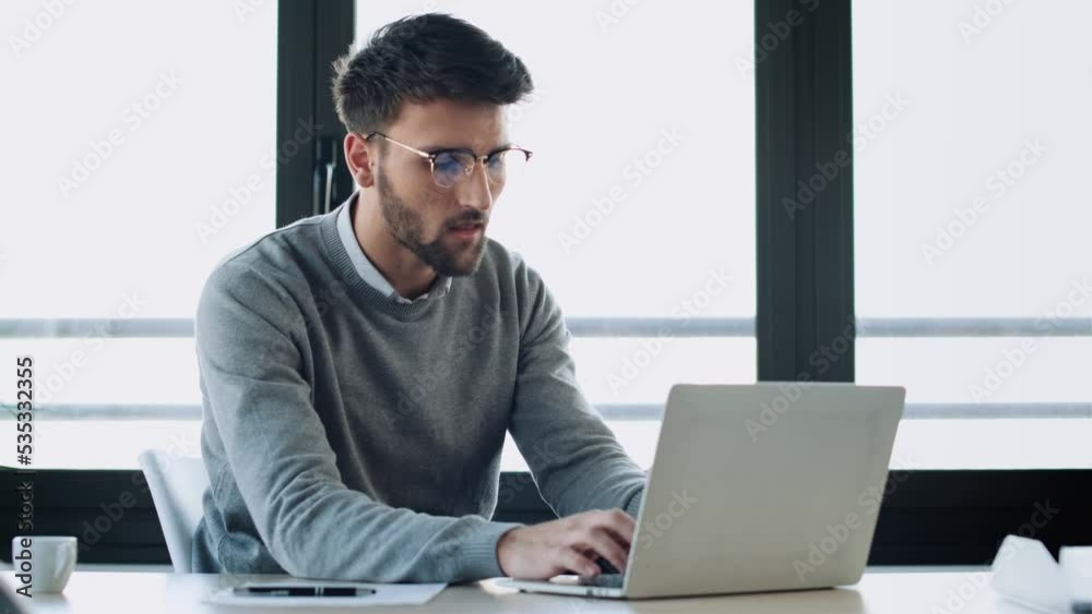 Video of handsome young entrepreneur working with computer while reading some documents in modern startup office. Video of handsome young entrepreneur working with computer while reading some documents in modern startup office.