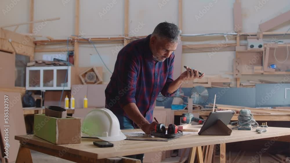 Mid adult man talking and writing while working in woodworking factory Mid adult man talking and writing while working in woodworking factory