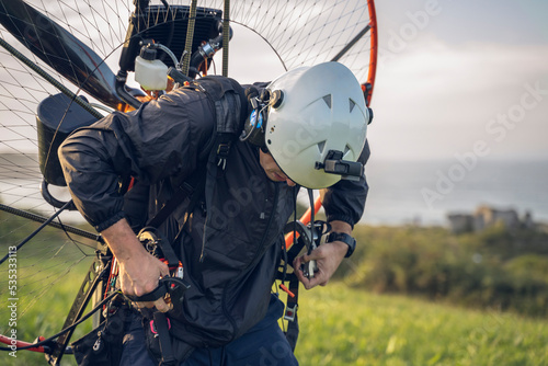 Young man, wearing a white helmet with an Action Cam on it, gets ready to fly with the Powered Paragliding ( PPG ) , and fastens his belt. In the background the Ocean.