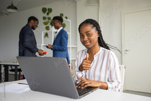 successful young woman in the office with a laptop with a hand gesture on the background of people