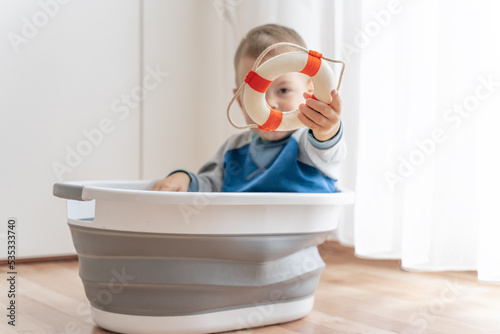 Kid play with toy boat and lifebuoy. Summer vacation and travel adventure concept. Child play in handmade ship with spyglass in hands, looking far, exploring horizon