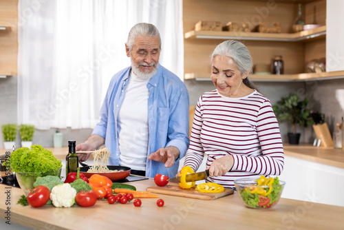 Portrait Of Cheerful Senior Spouses Preparing Lunch In Kitchen Together