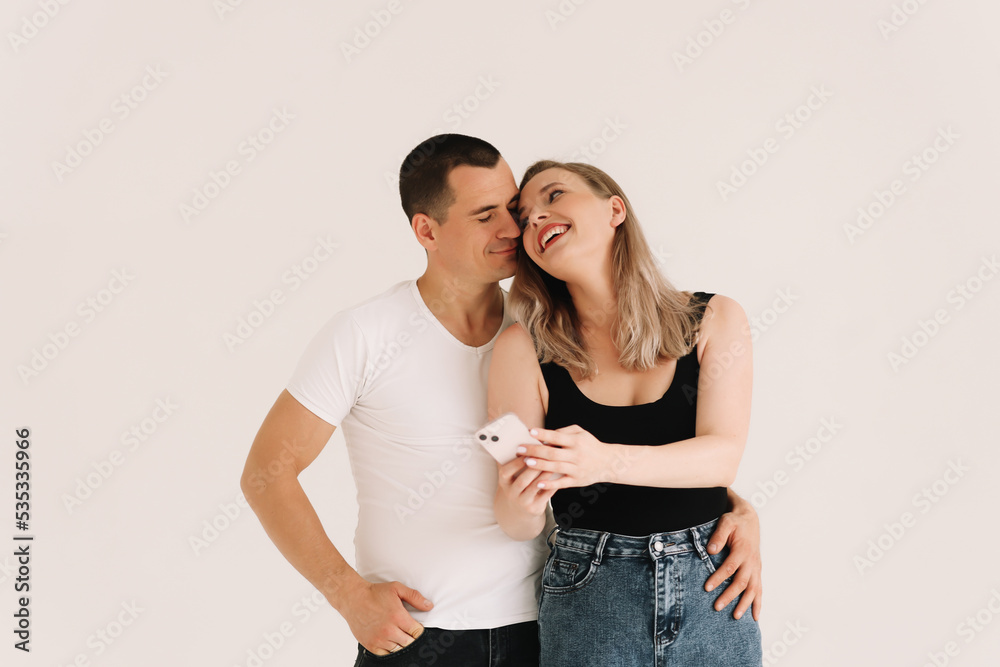 Two adults, a man and a woman in casual clothes, look into the phone, type a message, take a selfie using a mobile phone and technology on a white isolated background. Selective focus. Place for text Two adults, a man and a woman in casual clothes, look into the phone, type a message, take a selfie using a mobile phone and technology on a white isolated background. Selective focus. Place for text