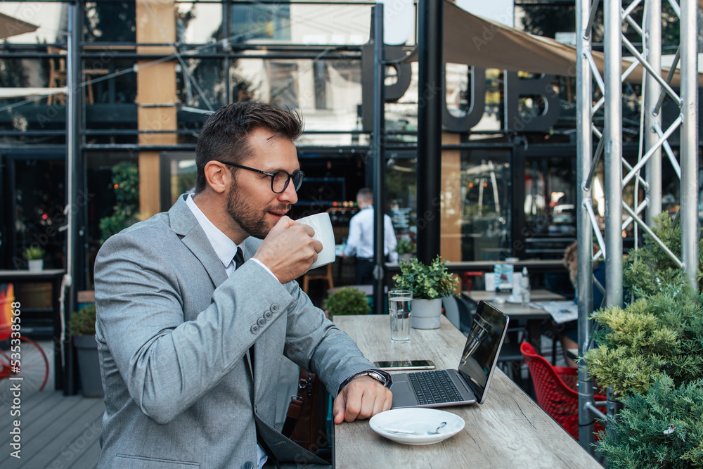 Middle age businessman sitting in cafe bar and enjoying at coffee break between two meetings. He uses laptop computer and he is positive and confident. Middle age businessman sitting in cafe bar and enjoying at coffee break between two meetings. He uses laptop computer and he is positive and confident.