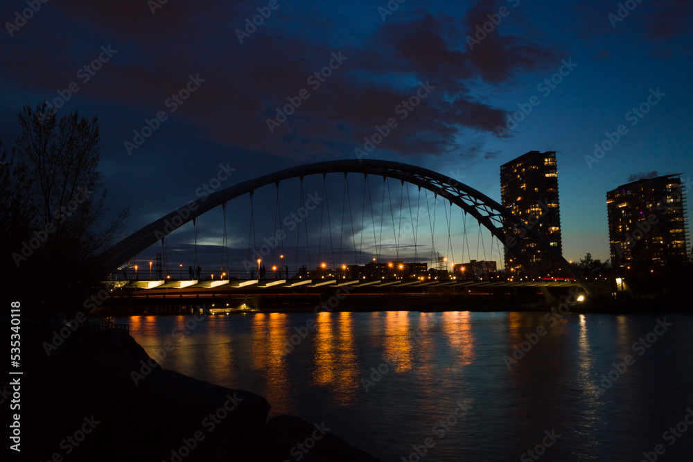 Evening city - arch suspension bridge, night lights, people walking and beautiful evening sky