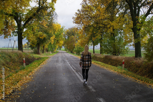Kobieta idąca ulicą wśród jesiennych drzew. © Adam Sadlak