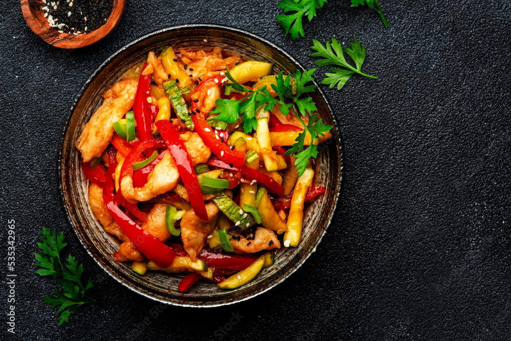 Asian cuisine, stir fry with chicken, red paprika pepper and zucchini bowl. Black kitchen table background, top view, copy space Asian cuisine, stir fry with chicken, red paprika pepper and zucchini bowl. Black kitchen table background, top view, copy space