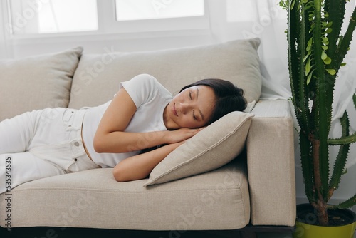 Young beautiful Asian woman sleeping on the couch at home with her eyes closed while lying on her side, resting and relaxing from stress while sleeping