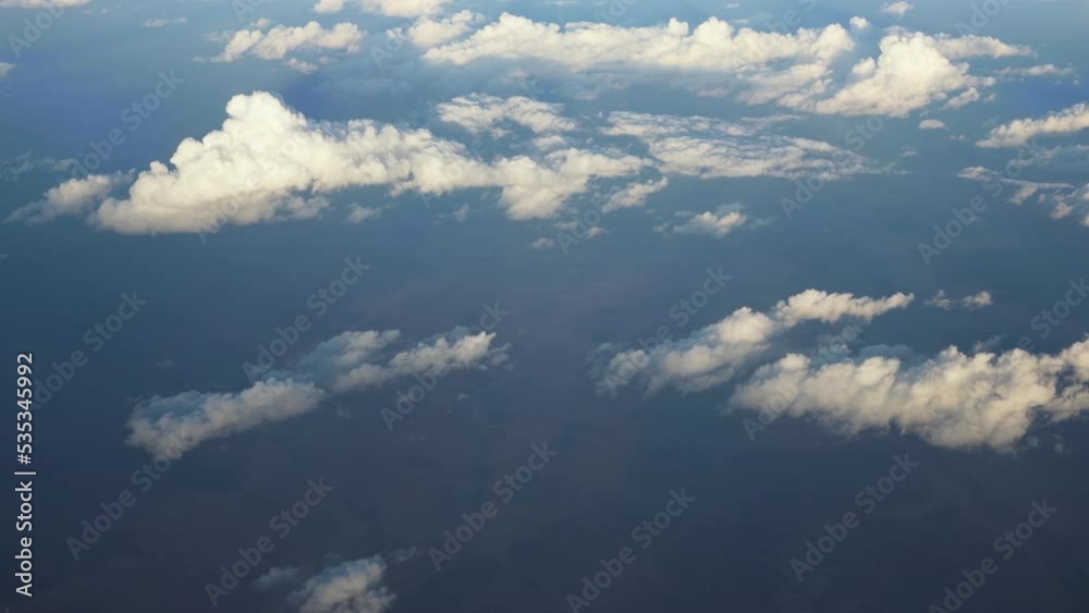 View from airplane window - flying over fluffy clouds lit by sun View from airplane window - flying over fluffy clouds lit by sun