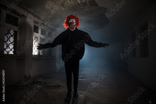 closeup of a scary evil clown with red hair and white eyes, staring at the observer, with a red balloon in front of him, against a black background