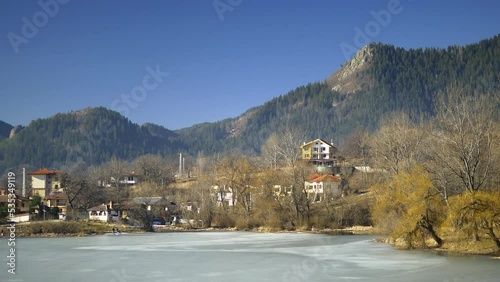 Panorama of a frozen pond with cottages in forest. A village at the Province of Plovdiv, Rhodope Mountains in Bulgaria. Beautiful lakeside nestled among colorful trees displaying autumn foliage
 photo