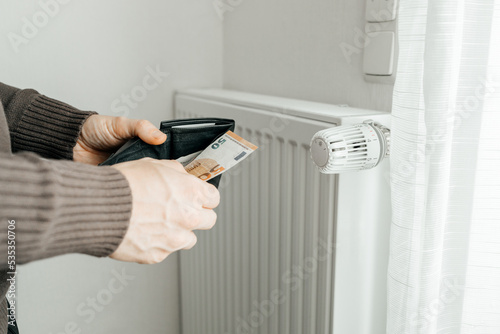 The man's hands hold a wallet with money next to the radiators. The concept of increasing prices for gas and energy. Energy crisis in Europe.