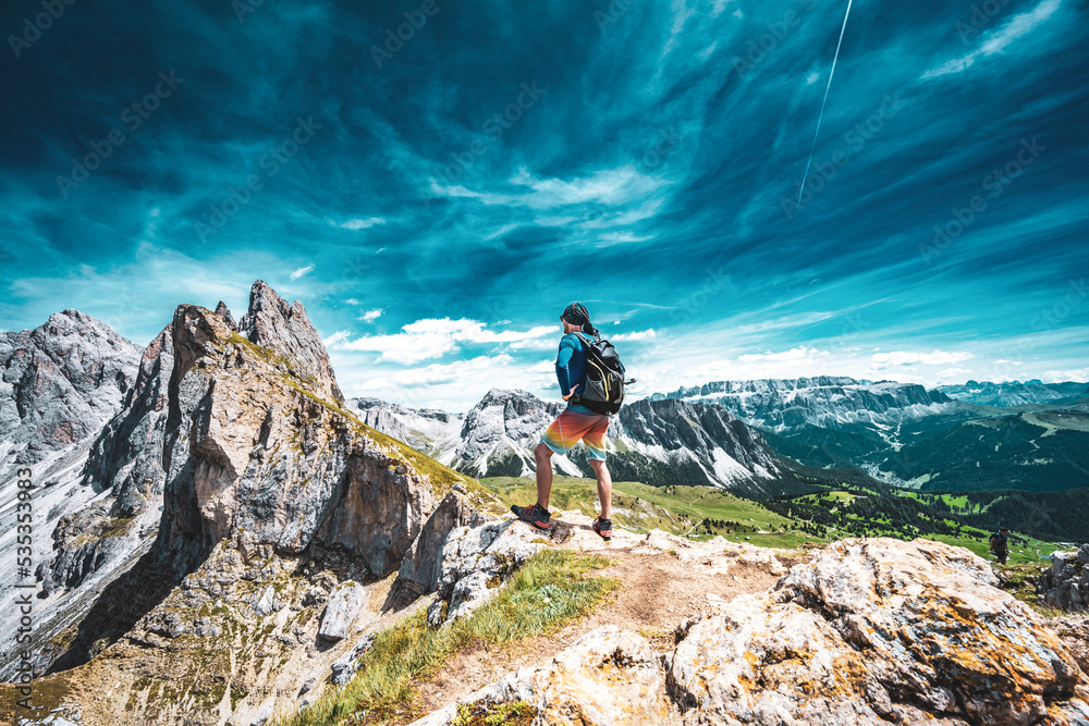 Athletic man stands at beautiful view point and enjoys view on Seceda in the dolomites in the afternoon. Seceda, Saint Ulrich, Dolomites, Belluno, Italy, Europe.