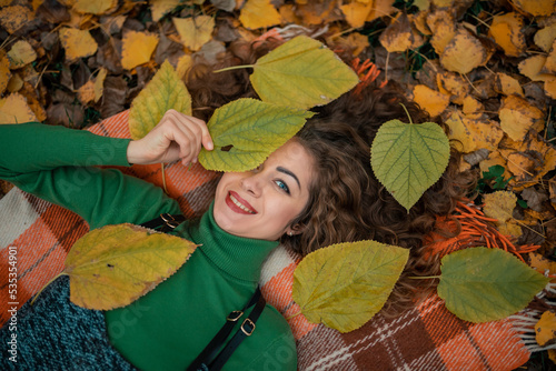 Beautiful girl liyng on autumn leaves and looks at the camera with a smile photo