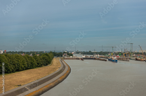 Brunsbuttel, Germany - July 12, 2022: Wide landscape under partly cloudy blue sky of Kiel Kanal locks with ships entering them. Gray North Sea water up front. Kiel Kanal bridge on horizon