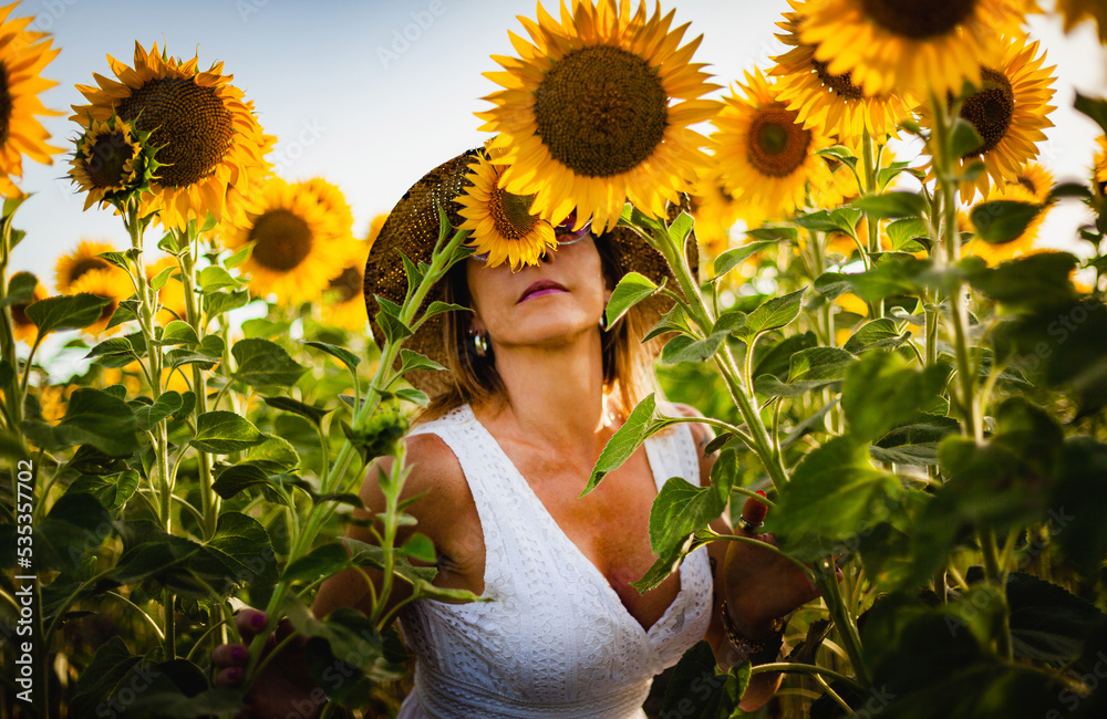 beautiful woman smelling the scent of nature in a field of sunflowers in el puerto de santa maria, andalusia spain. - obrazy, fototapety, plakaty 