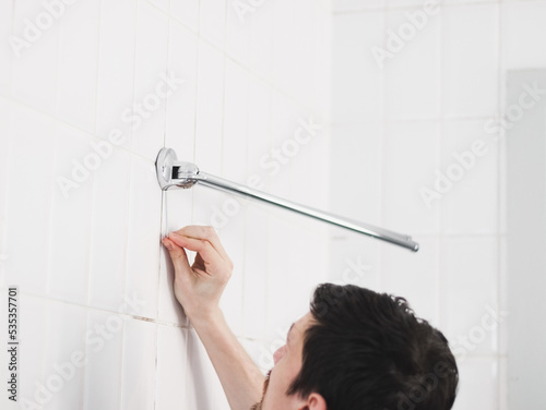 A young Caucasian guy unscrewing a screw with a small hex wrench to take off an old metal hanger
