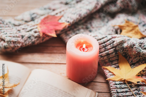 Burning candle  open book  autumn leaves and knitted sweater on wooden table. Fall concept. Top view