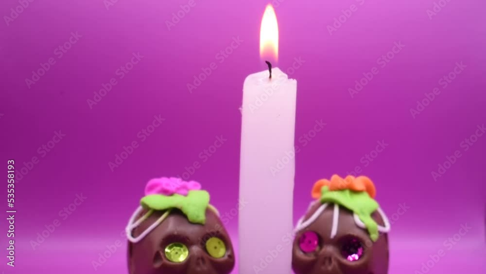 altar de dia de muertos con dos calaveras de chocolate y una vela de cera encendida en un fondo morado 