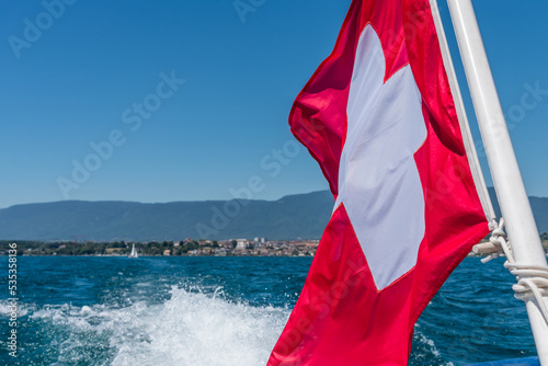 Swiss flag fluttering in the wind from the stern of a ship with the wake on Lake Geneva