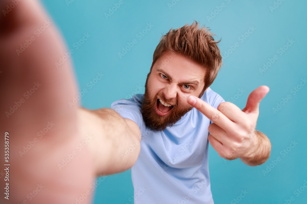 Φωτογραφία Portrait of bearded man blogger POV, making point of view of photo, showing middle finger to camera, expressing anger and aggressive emotions