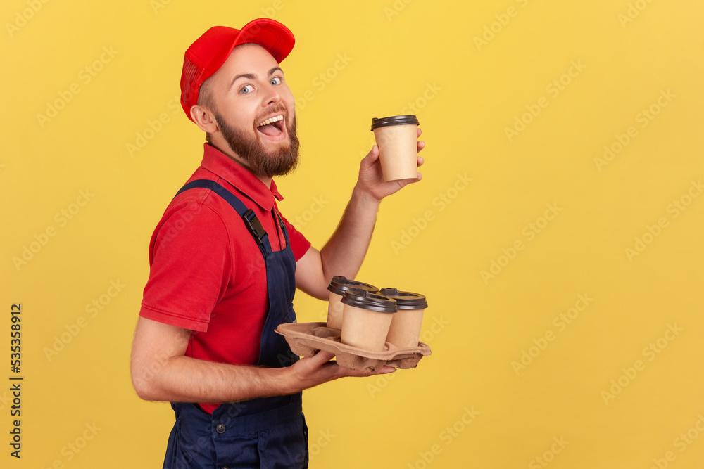 Φωτογραφία Side view portrait of excited amazed delivery man standing with take away coffee and drinking hot beverage, looking at camera and laughing