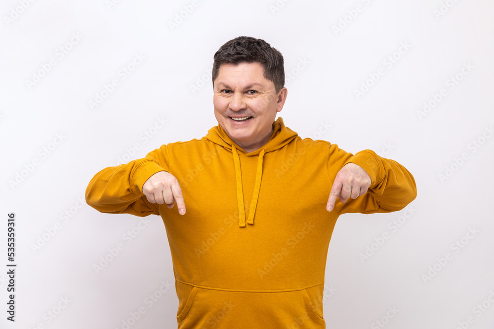 Cheerful delighted man pointing fingers down, paying attention to advertising area, blogger recommending to subscribe, wearing urban style hoodie. Indoor studio shot isolated on white background. Cheerful delighted man pointing fingers down, paying attention to advertising area, blogger recommending to subscribe, wearing urban style hoodie. Indoor studio shot isolated on white background.