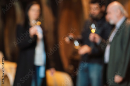 Blurred wine cellar guests, one woman and two men tasting a white wine produced and aged by an old traditions in oak barrels