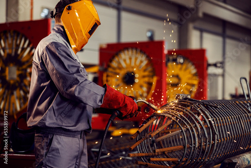 A metallurgy worker welds metal framework with a welding machine in the factory.