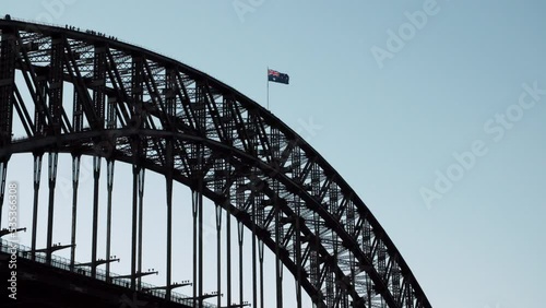 The Australian flag flying high on a bridge while climbers ascend its heights.