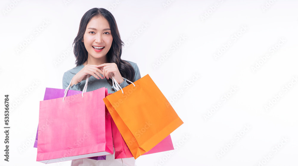 Enjoyment excited asian woman carry shopping bags standing on white background. Trendy happy shopper consumer carefree young girl holding shopping paper bags with copy space over isolated background.