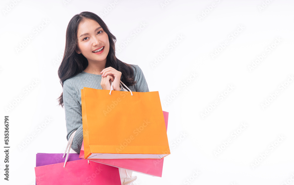 Enjoyment excited asian woman carry shopping bags standing on white background. Trendy happy shopper consumer carefree young girl holding shopping paper bags with copy space over isolated background. Enjoyment excited asian woman carry shopping bags standing on white background. Trendy happy shopper consumer carefree young girl holding shopping paper bags with copy space over isolated background.