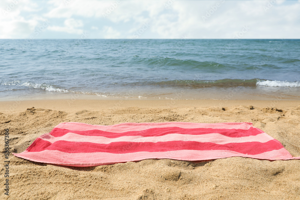 Pink striped towel on beach sand near sea Pink striped towel on beach sand near sea