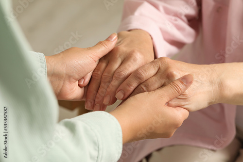 Young and elderly women holding hands indoors, closeup