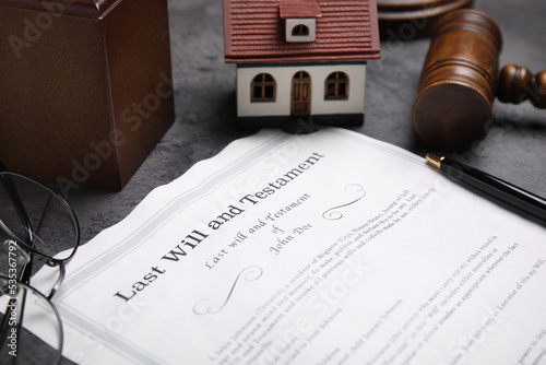 Last will and testament near house model, glasses and gavel on grey table, closeup