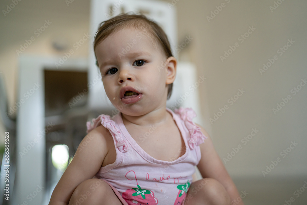 One child squatting with messy mouth at home in the living room Early development learning and playing concept one girl baby toddler alone in summer day front view copy space