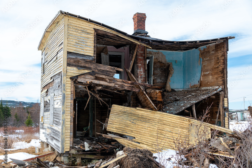 The interior of a building being demolished. The walls are layers of blue paint, wallpaper and wood. There's an open single white wooden door in the house. The room is covered in dirt and materials. The interior of a building being demolished. The walls are layers of blue paint, wallpaper and wood. There's an open single white wooden door in the house. The room is covered in dirt and materials.