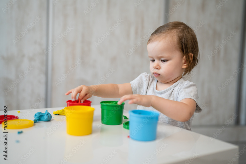 One girl small caucasian toddler child playing with colorful plasticine on the table at home alone childhood and growing up development concept copy space One girl small caucasian toddler child playing with colorful plasticine on the table at home alone childhood and growing up development concept copy space