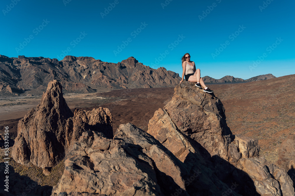 Girl sitting on the rocks in Teide National Park. Volcanic landscape. Roques de García trail. Tenerife, Canary islands, Spain.