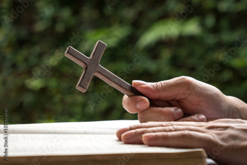 Man holding a wooden religious cross crucifix with an open bible. Close up view.