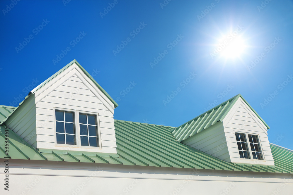 dormer with windows on metal sheet roof with blue sky and sunshine.